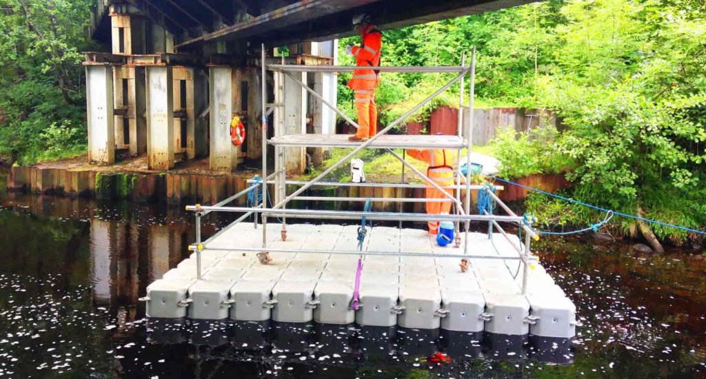 Scaffold tower on a handrailed modular pontoon platform beneath a bridge deck for inspection access