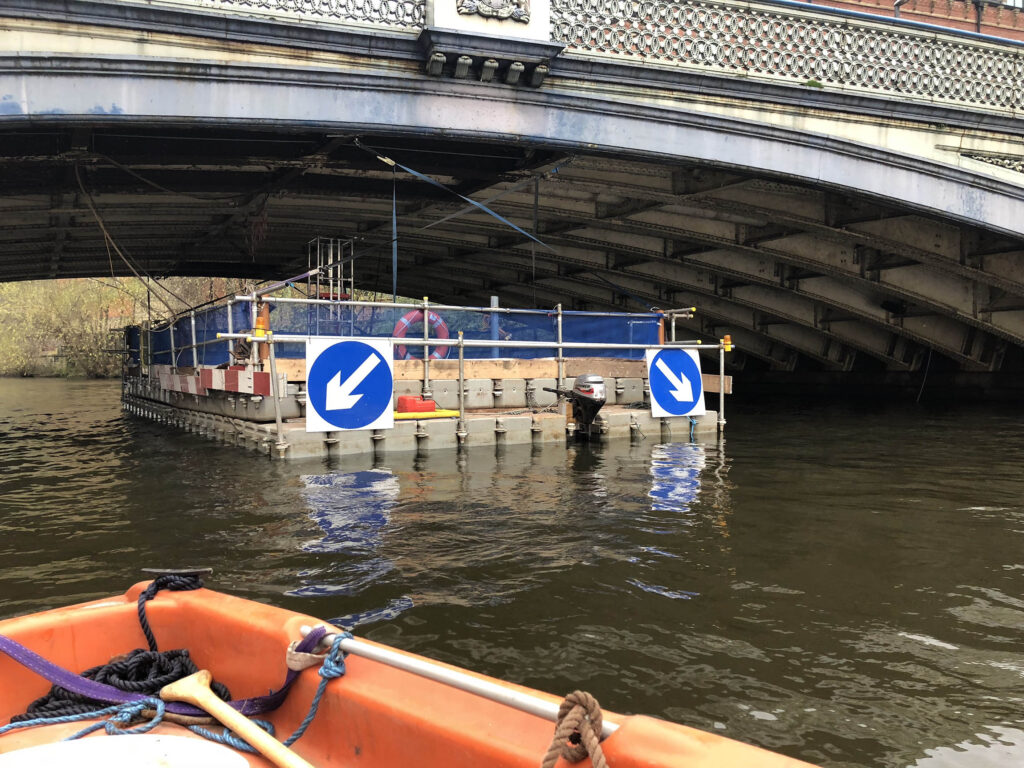 Modular floating pontoon platform with navigation signs and an outboard motor positioned under an arched road bridge